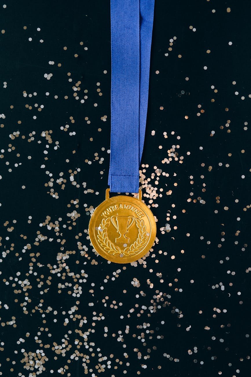 Photo by Nataliya Vaitkevich on <a href="https://www.pexels.com/photo/close-up-shot-of-a-gold-medal-on-a-black-surface-6120397/" rel="nofollow">Pexels.com</a>